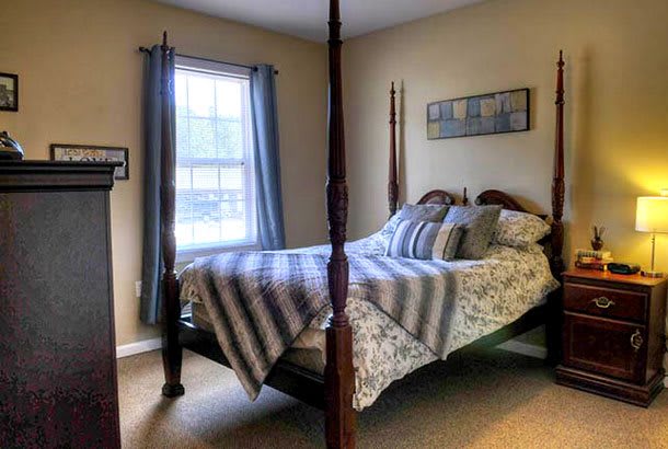 A cozy bedroom featuring a four-poster bed and a window with blue curtains.