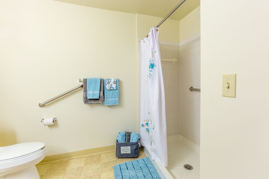 A bathroom with a shower, blue towels, and a safety grab bar.
