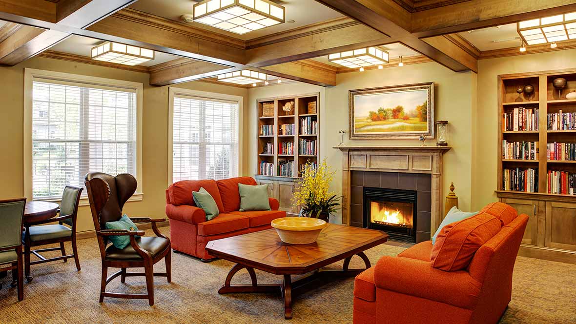 A cozy living room featuring vibrant orange sofas, a wooden coffee table, and a warm fireplace, with bookshelves and decorative artwork enhancing the inviting atmosphere.