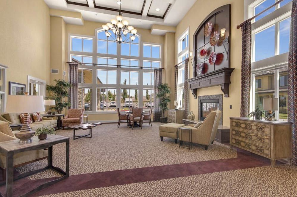 A spacious and cozy living room with a large chandelier, comfortable seating, and a fireplace, enhanced by natural light from big windows.