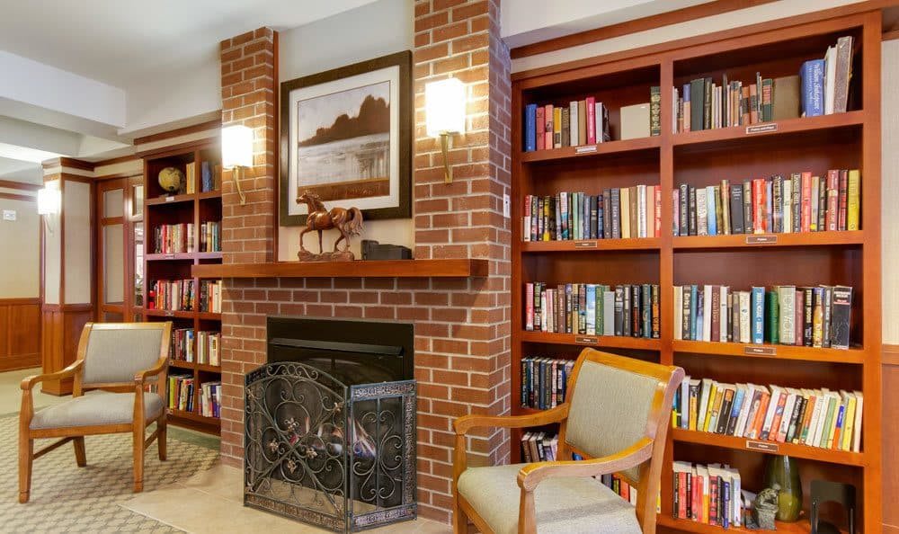 A cozy living room with a brick fireplace, surrounded by bookshelves and an armchair.