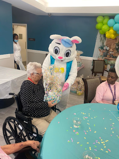 A festive Easter celebration featuring a bunny mascot interacting with residents at a senior care facility.