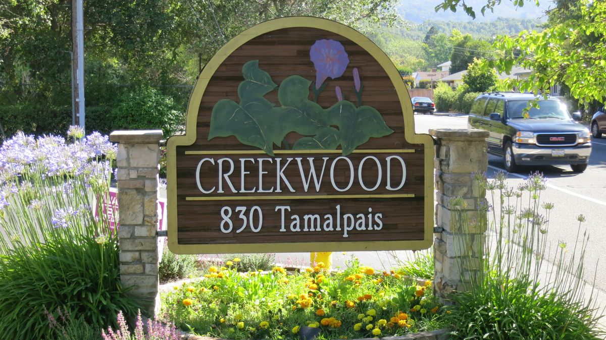 A Creekwood sign with an address displayed in a natural setting.