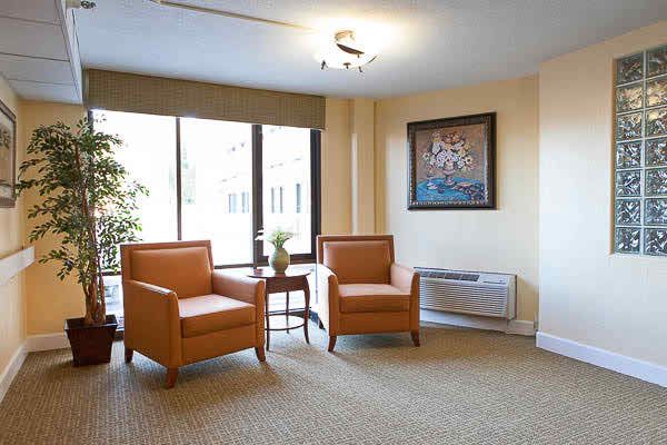 A cozy living room with two orange chairs, a small table, and a large window beside an artwork piece on the wall.