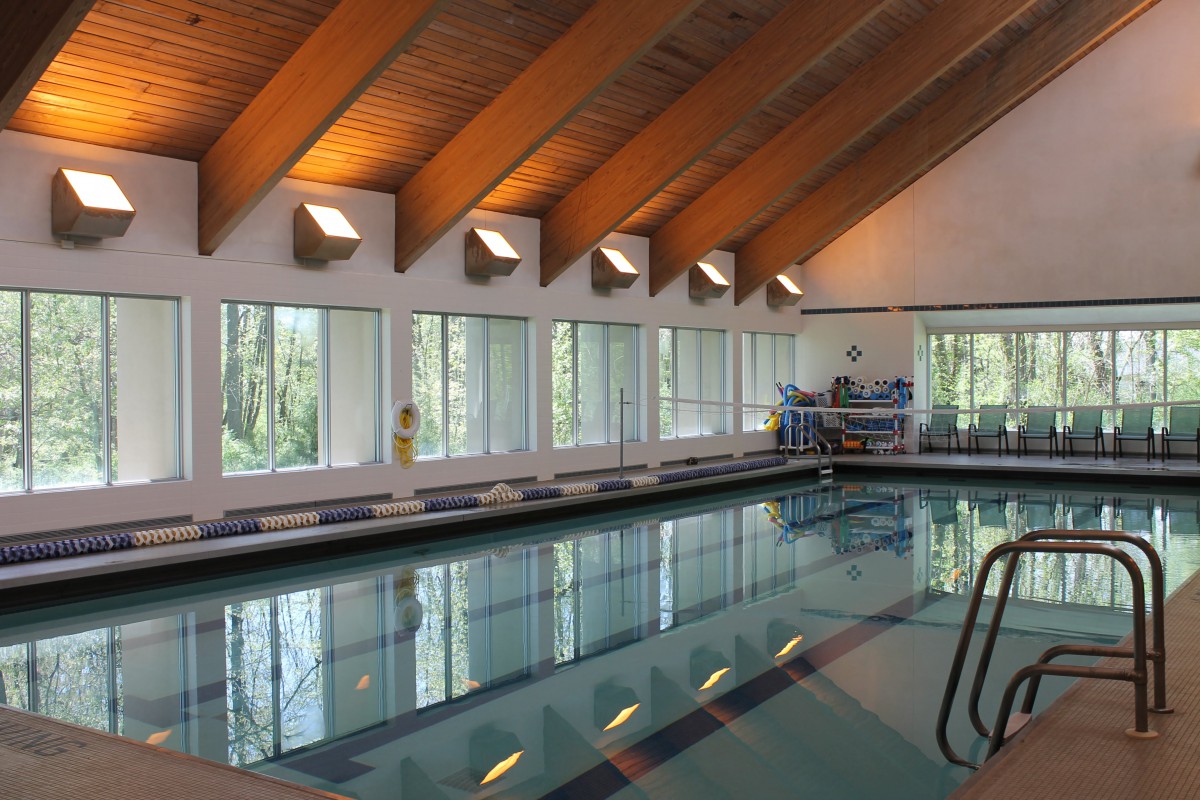 A serene indoor swimming pool with large windows and a wooden ceiling, allowing natural light to fill the space.