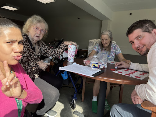 A group of people, including elderly individuals, gathered around a table engaging in conversation and activities.