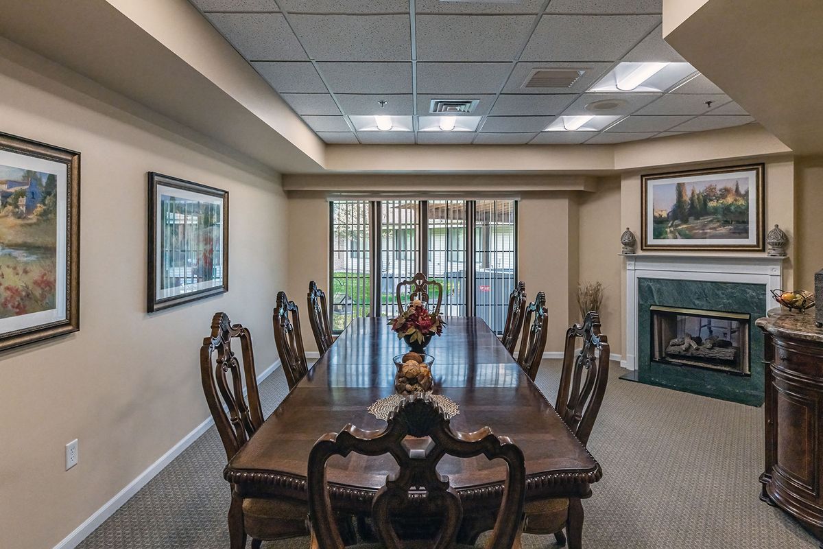 A well-appointed dining room with a large wooden table and elegant chairs, featuring decorative wall art and ample natural light from sliding glass doors.