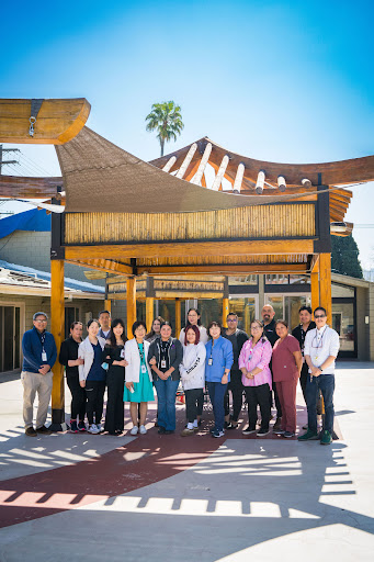 A diverse group of staff members gathered outdoors under a culturally-inspired structure, showcasing unity and community spirit.