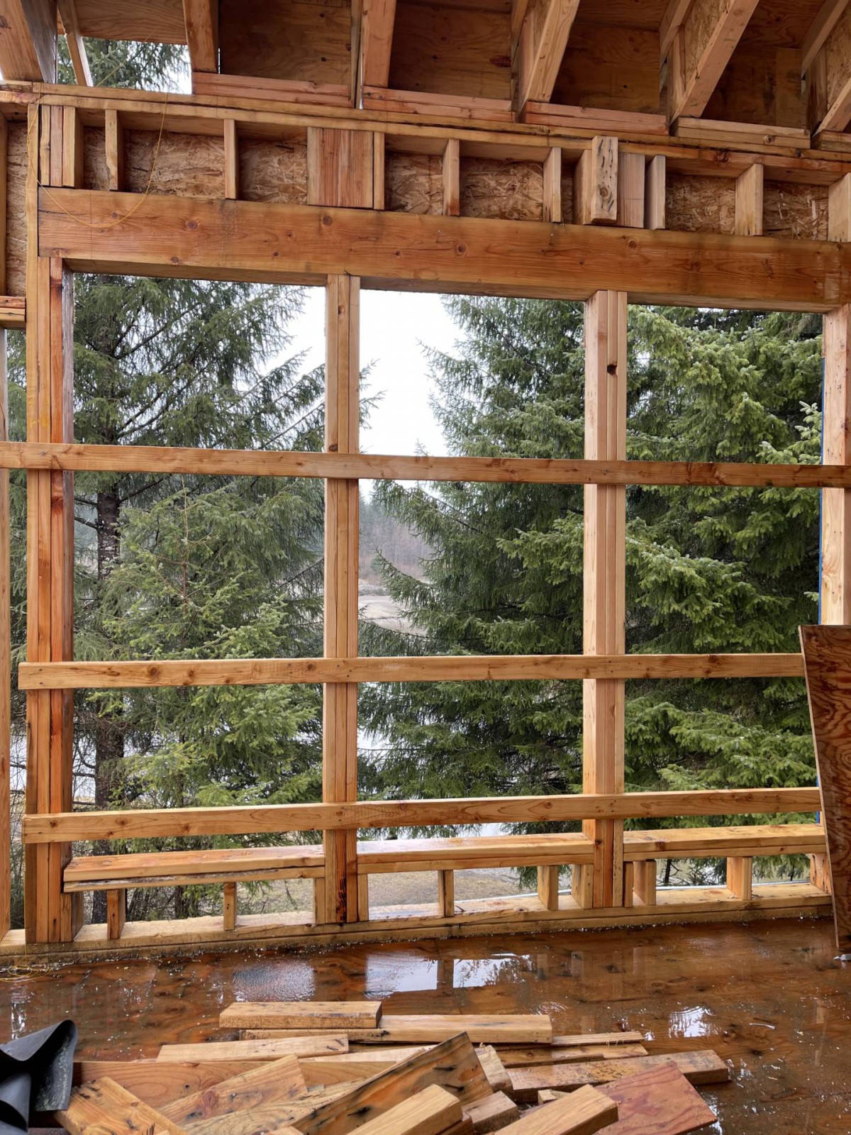 Partially constructed wooden window frame overlooking a forested area.