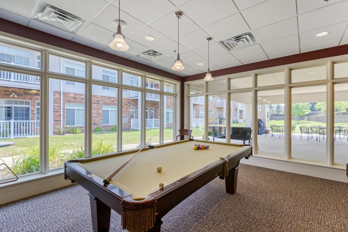 A bright and spacious billiards room with a classic pool table, large windows, and stylish pendant lighting.