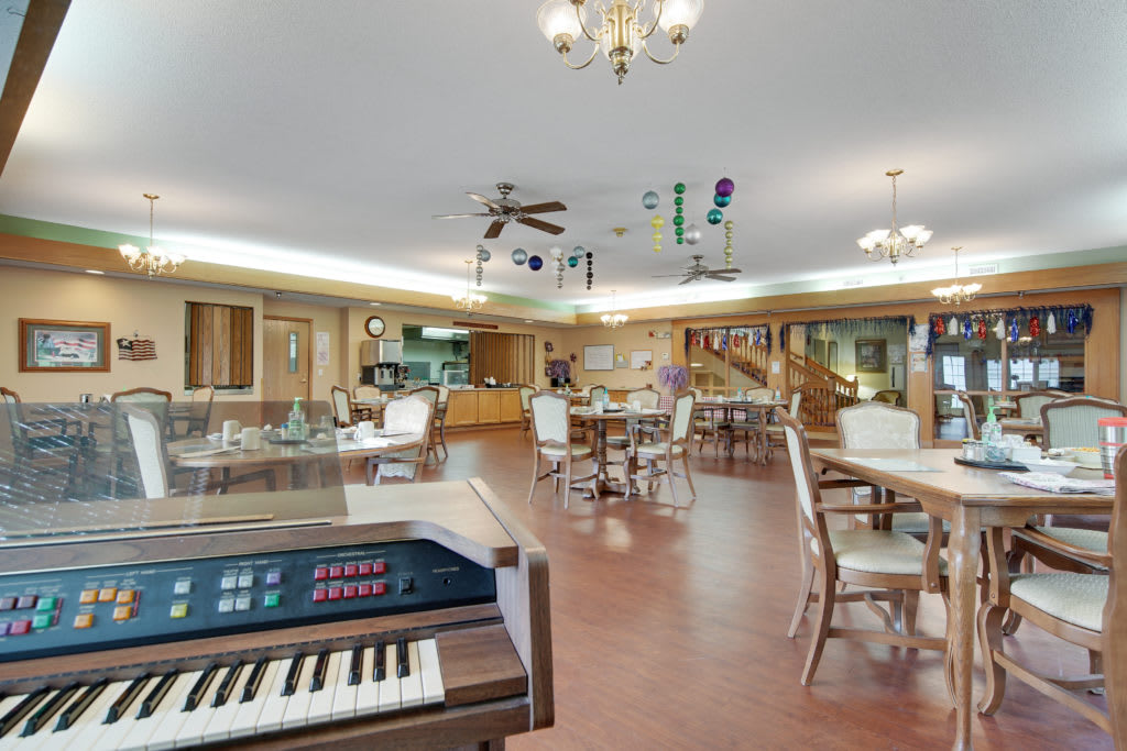 A spacious dining area featuring a piano, tables, and chairs under elegant lighting.