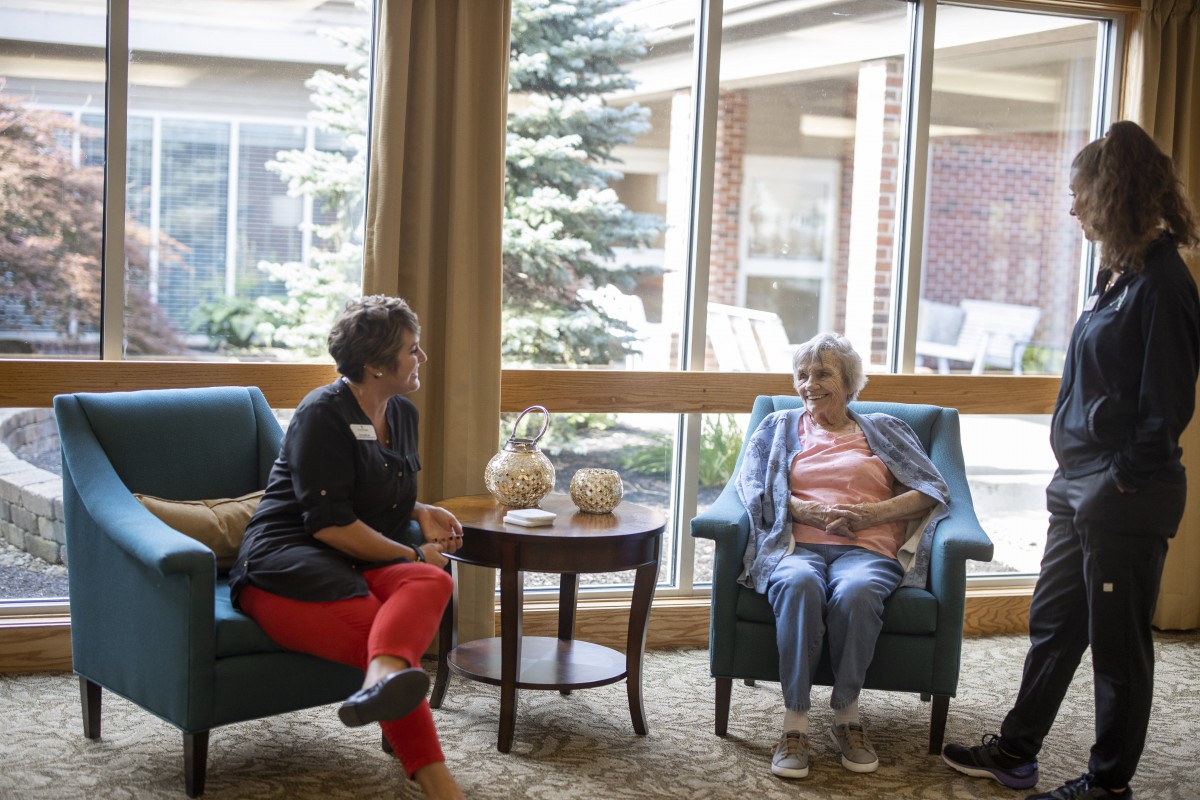 Two women engaged in a conversation in a comfortable indoor setting, possibly a senior living facility.
