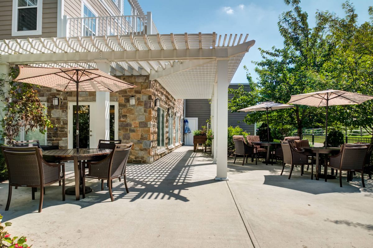 A sunlit patio with comfortable outdoor seating and a pergola above.