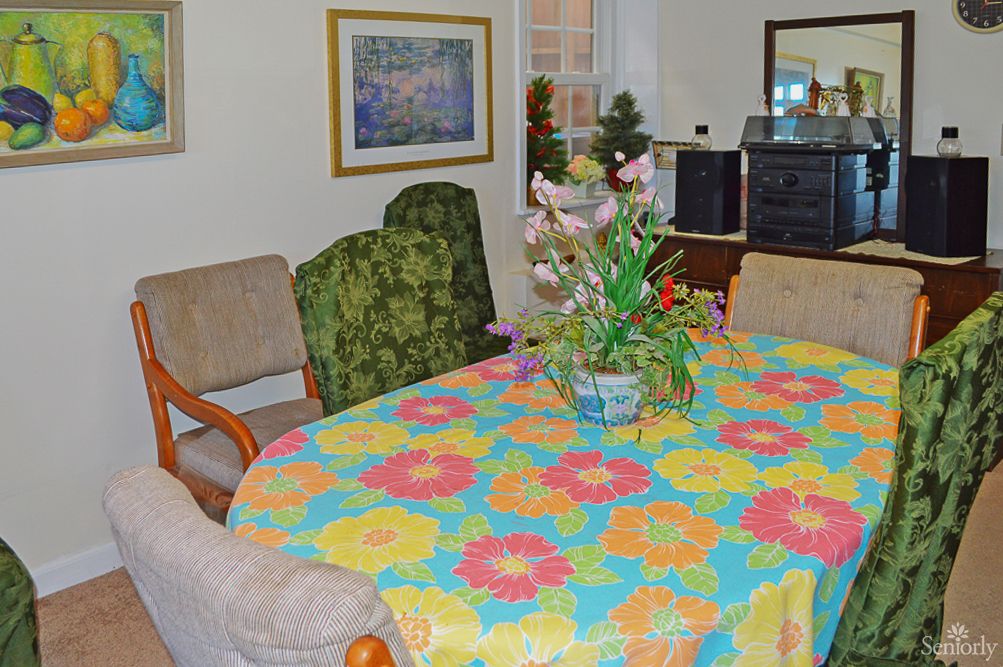 A cozy dining room featuring a brightly colored floral tablecloth and an arrangement of plants.