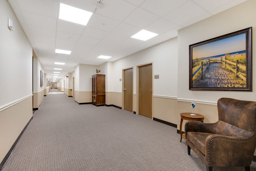 A well-lit hallway in an office setting with several closed doors and artwork on the walls.