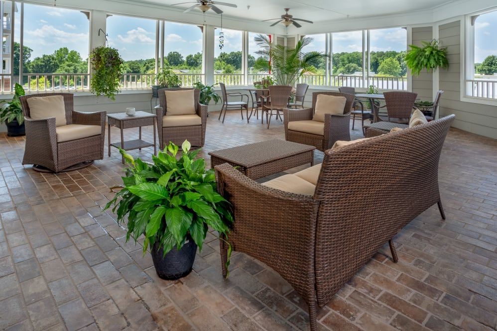 A cozy and elegant outdoor seating area with wicker furniture and lush greenery on a screened patio.
