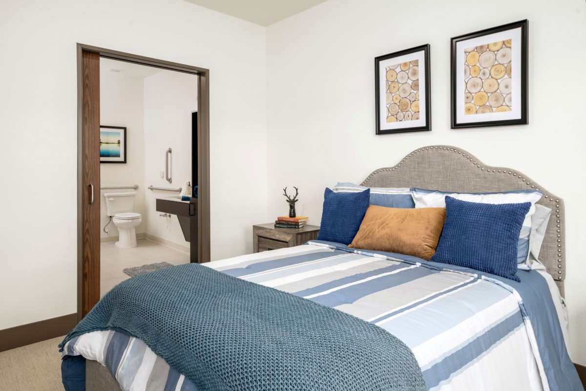 A cozy bedroom interior with a neatly made bed featuring striped bedding and decorative pillows, adjacent to a bathroom.