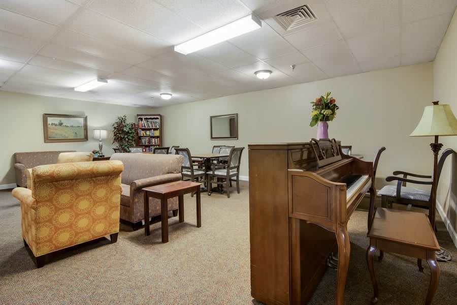 A cozy living room featuring a piano, sofas, tables, and bookshelves.