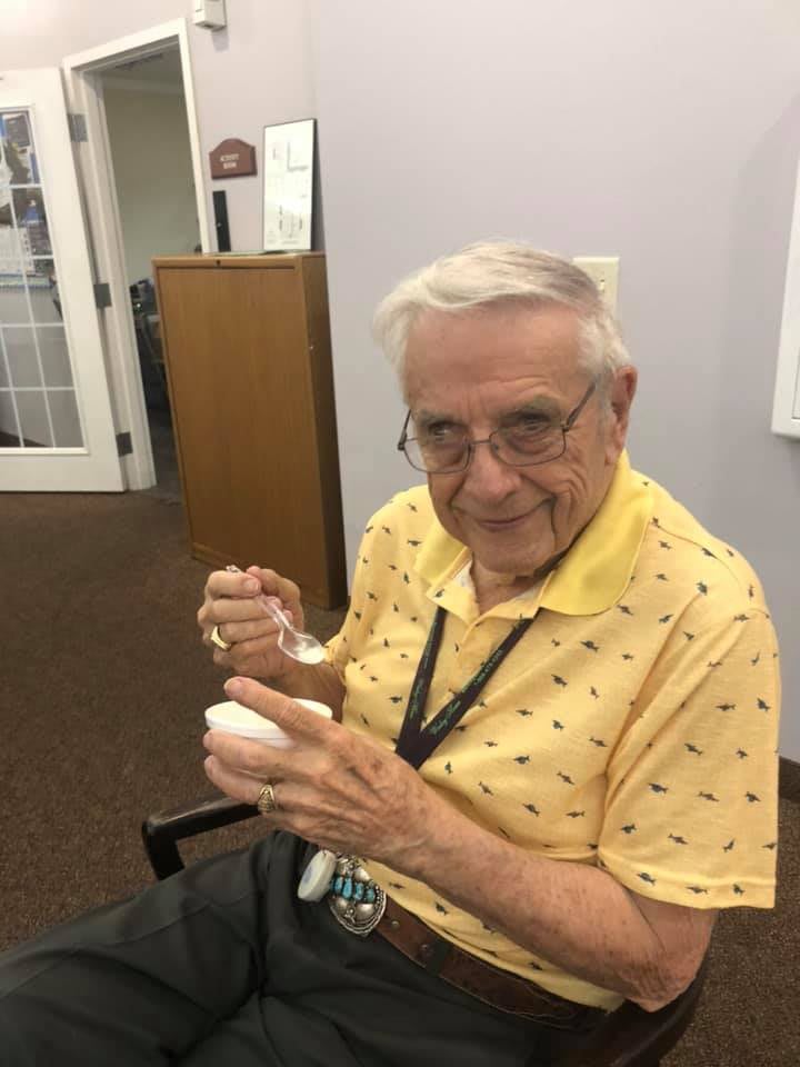 An elderly man enjoys a bowl of ice cream indoors.