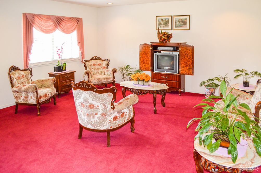 A vintage-style living room with floral upholstered furniture, a red carpet, and a classic television set.
