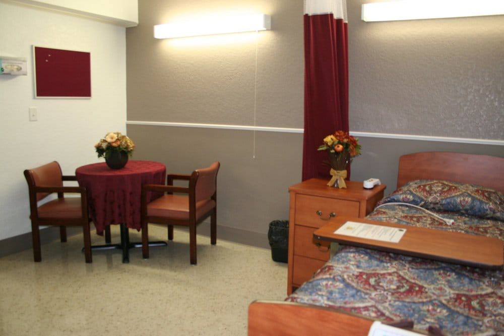 A cozy bedroom with a bed, small table, chairs, and decorative flowers.