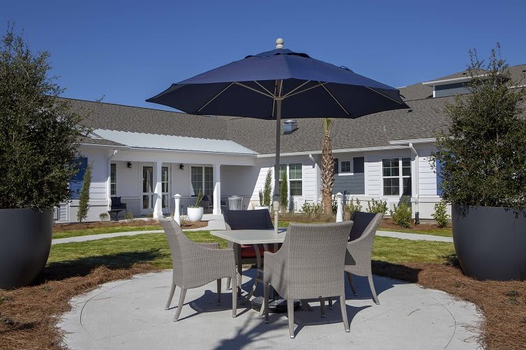 A patio with a table and chairs under a blue umbrella in a backyard setting.