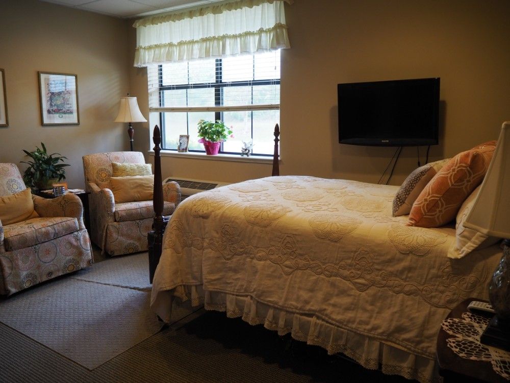 A cozy bedroom featuring a neatly made bed, an armchair by the window, and a wall-mounted television.