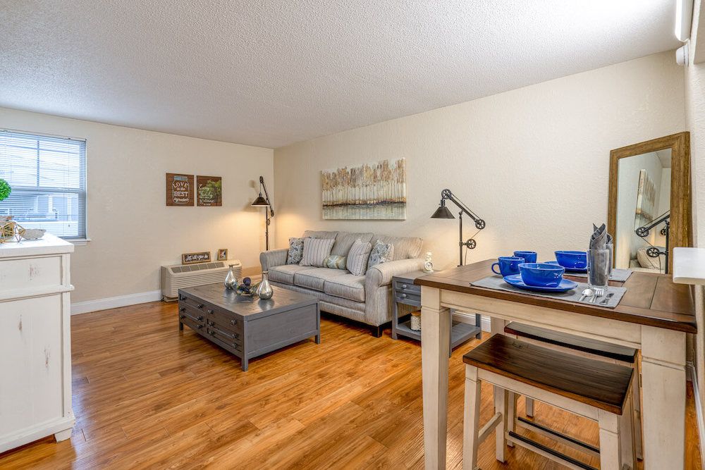 A cozy living room with a sofa, coffee table, and dining area, featuring warm wood flooring and stylish decor.