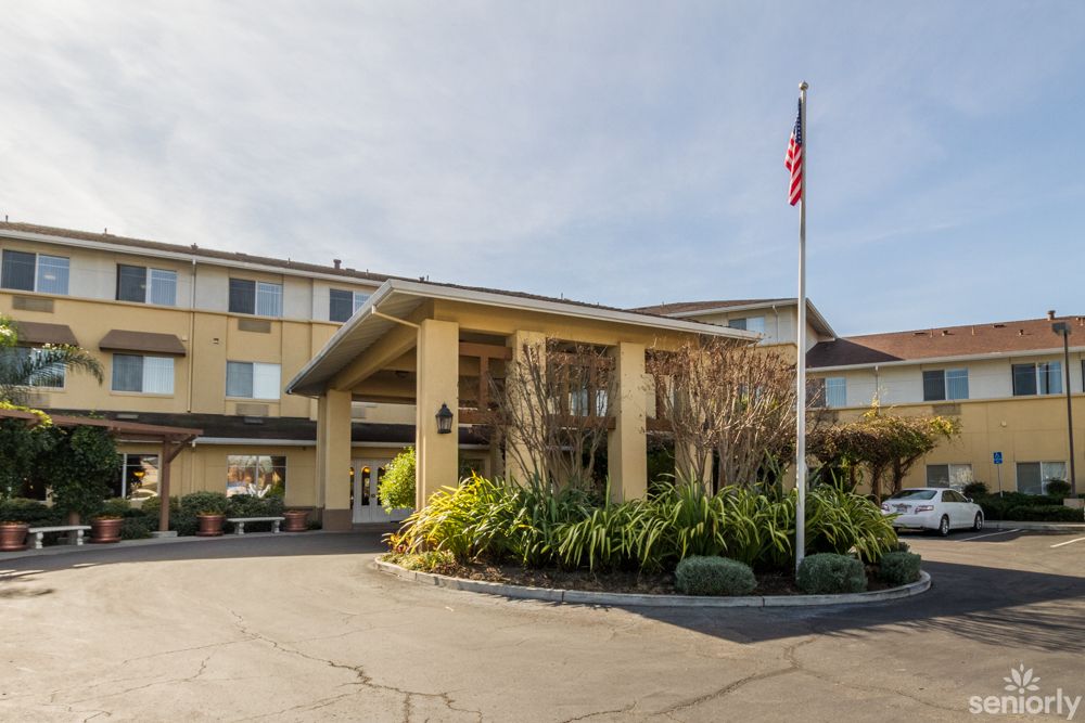 The exterior view of a hotel with an entrance surrounded by well-maintained landscaping and a flagpole.