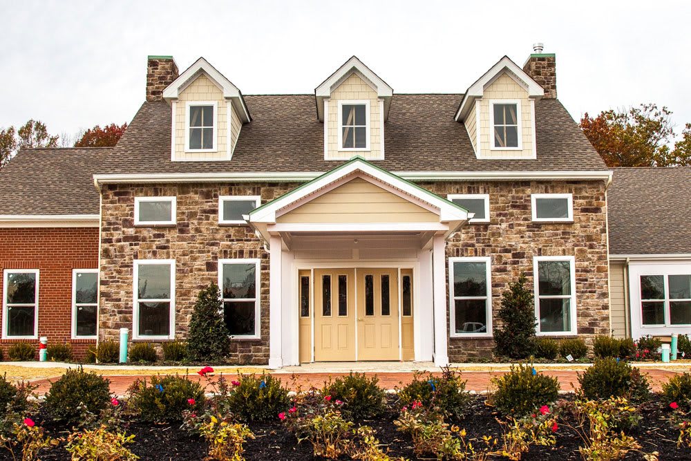 A classic stone facade house with symmetrical windows and a welcoming porch surrounded by landscaped gardens.