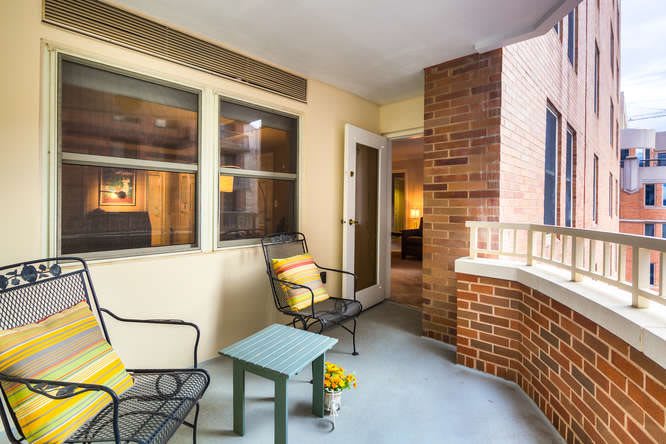 A cozy balcony with chairs and a table, featuring a view into an apartment through large windows.