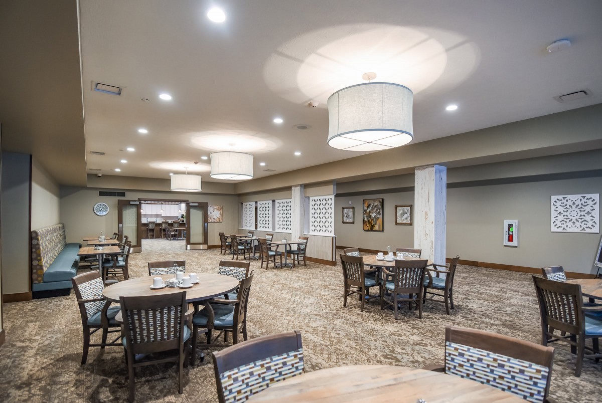 A spacious dining area with round tables, chairs, and modern lighting fixtures.