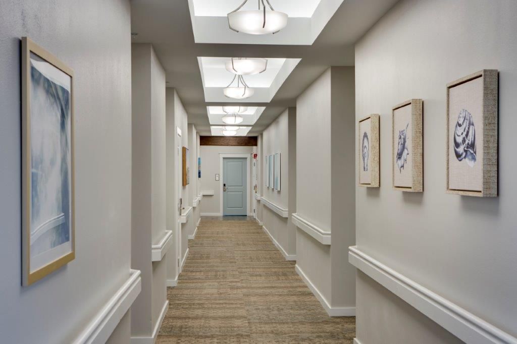 A well-lit, modern hallway with framed artwork on the walls and a central elevator.