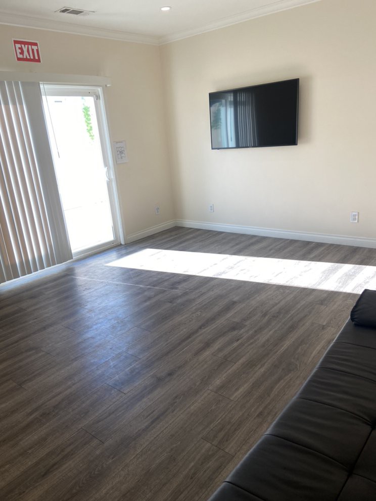 A minimalist living room with natural lighting, featuring a wall-mounted television and hardwood floors.