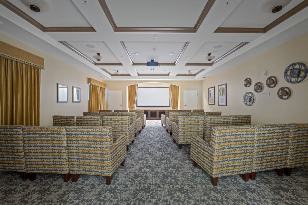 A well-furnished conference room with a projector screen and upholstered chairs arranged in rows.
