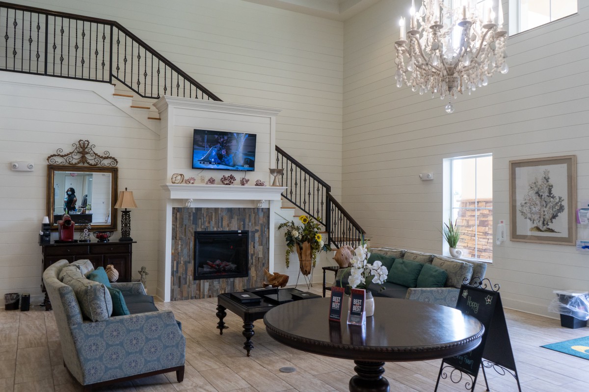 A spacious living room featuring a grand chandelier, elegant staircase, and cozy seating area around a fireplace.