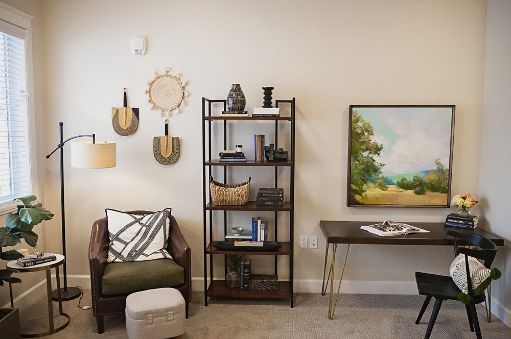 A modern living room featuring a shelving unit with decor, a cozy chair, and wall art.