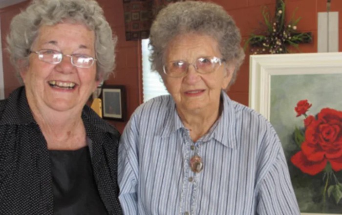 Two elderly women smiling together indoors.