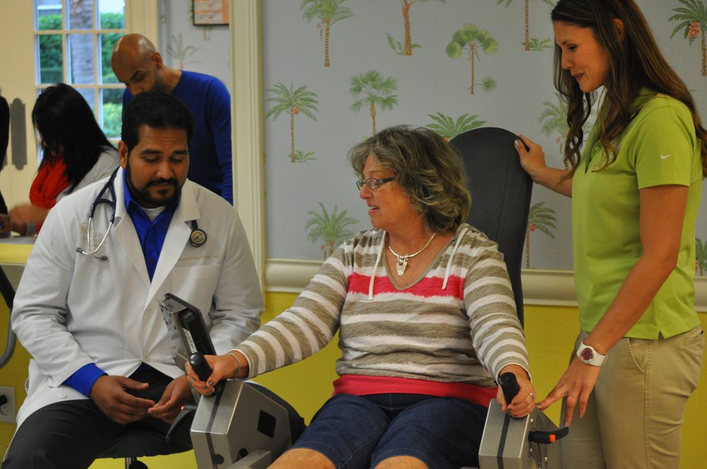 A senior woman receiving guidance from healthcare professionals during a physical therapy session using exercise equipment.