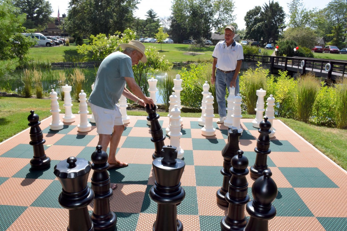 Two people engage in a game of giant chess at a park.