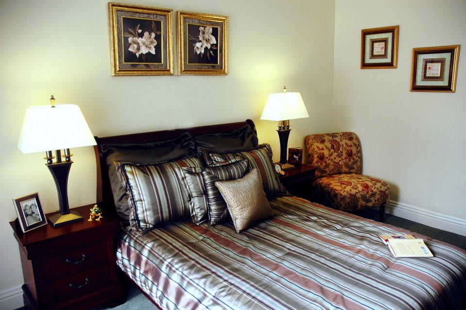A well-decorated bedroom featuring a neatly made bed with striped bedding, accent pillows, bedside tables with lamps, and framed artwork on the walls.