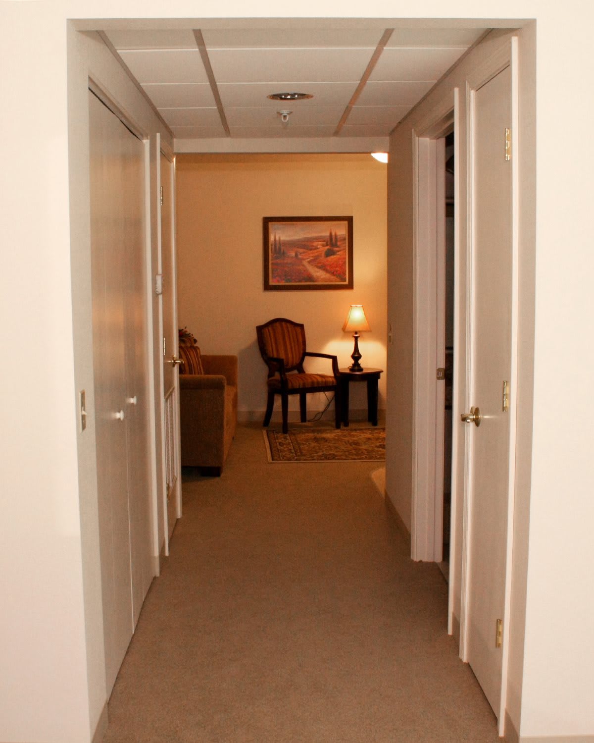 A well-lit hallway with doors on either side leading to a warmly furnished room.