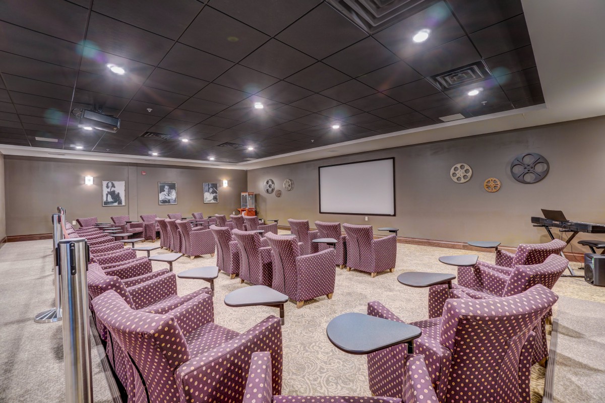 A well-lit auditorium with rows of comfortable seating facing a large screen.