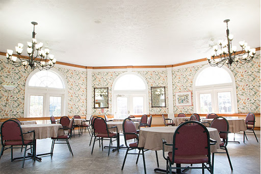 A spacious dining area featuring round tables and comfortable chairs, illuminated by natural light from large windows.