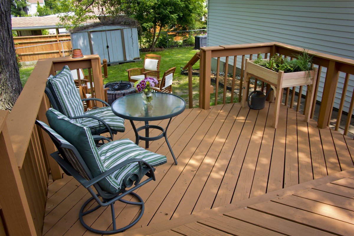 A cozy backyard deck featuring outdoor seating with striped cushions and a round glass table.