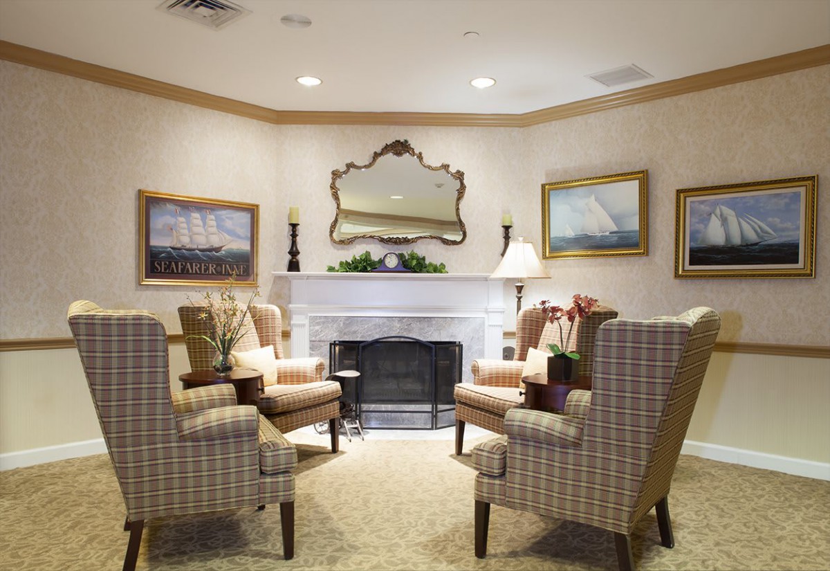 A cozy living room with elegant chairs arranged around a fireplace, complemented by a large mirror and framed paintings on the walls.