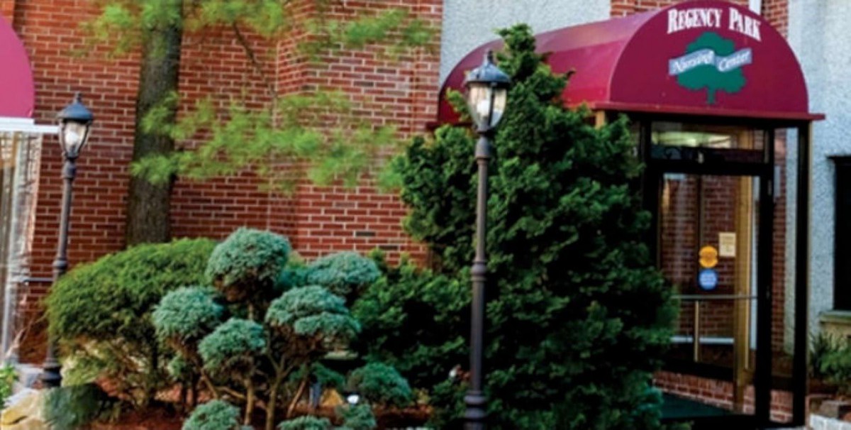 A charming street corner with a vintage lamp post surrounded by lush greenery and red brick architecture.