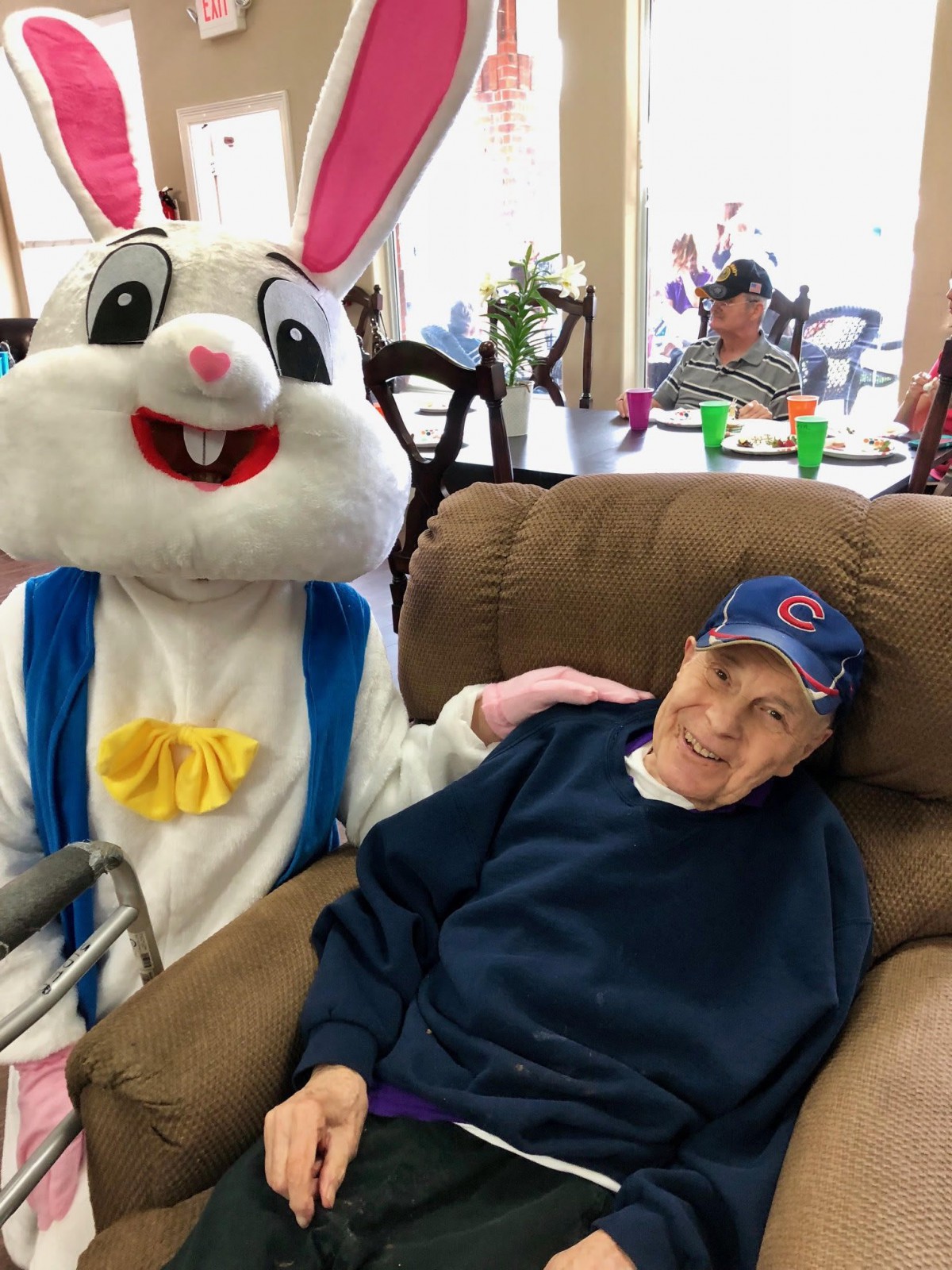 An Easter Bunny visits a nursing home, sharing a moment with an elderly resident in a recliner.