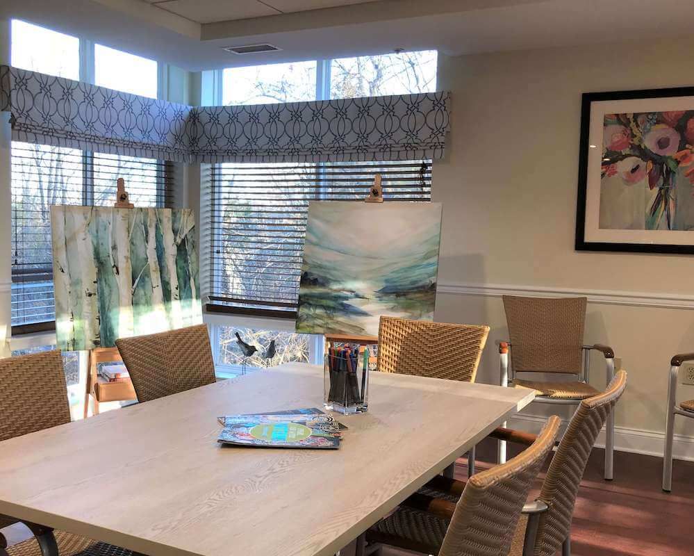 A well-lit art studio with paintings displayed on easels and art supplies on the table.