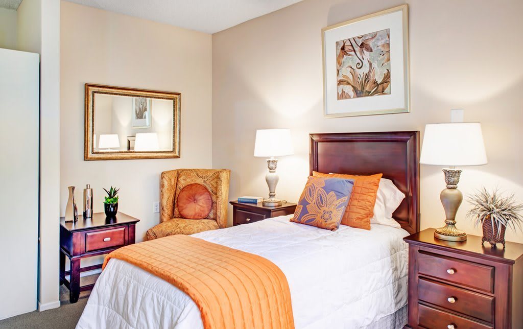 A cozy bedroom featuring a single bed with orange accents and elegant decor.